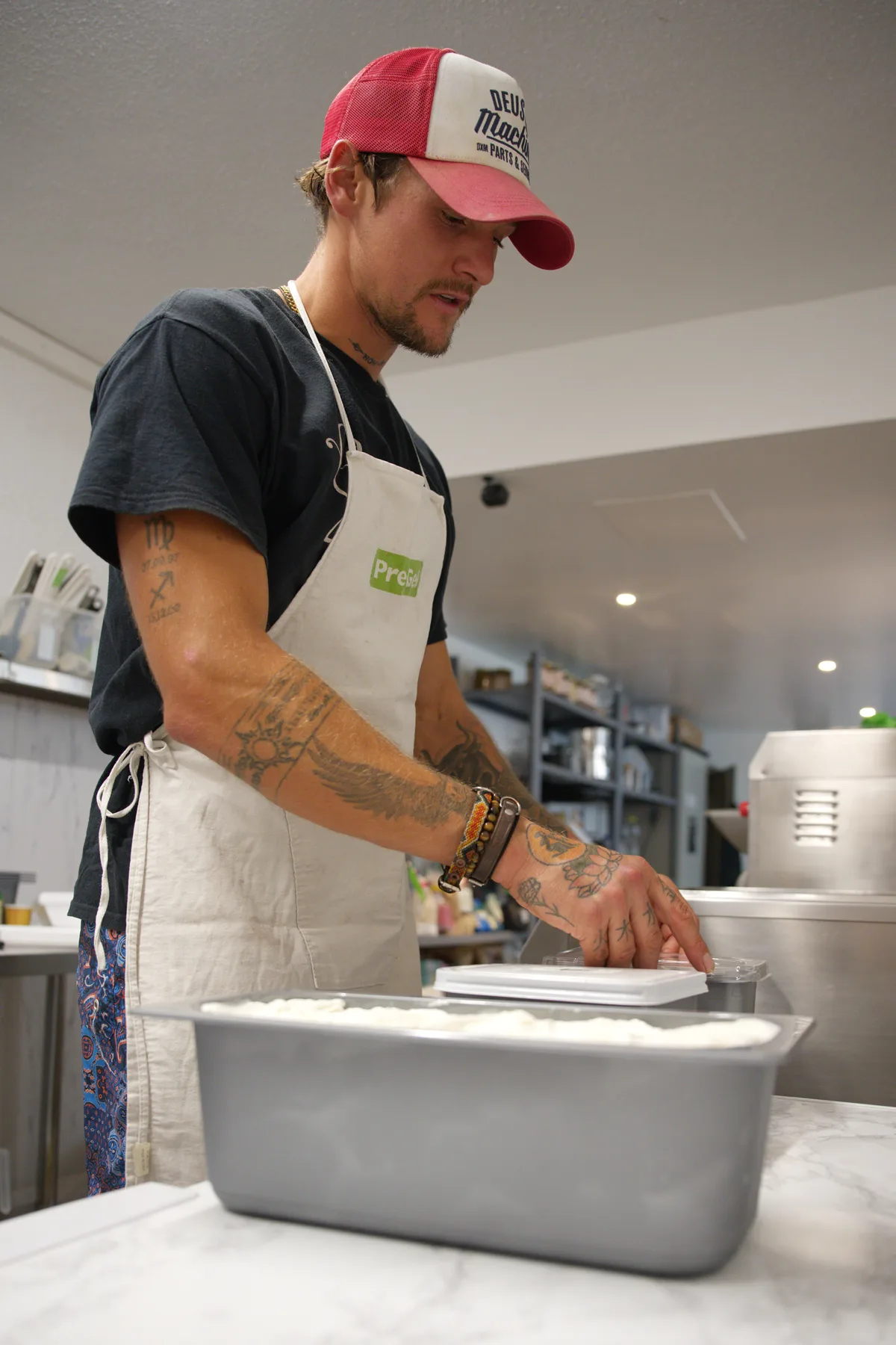 … verschliessen, fertig. Nach Bedarf werden vorher noch weitere Zutaten in die Glace gegeben. Ein Mann steht vor einem Tisch, wo Glacebehälter darauf stehen.